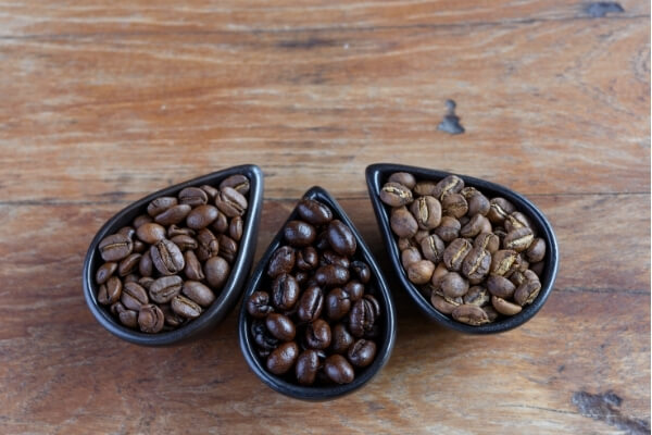 braune, dunkelbraune und hellbraune Kaffeebohnen in drei verschiedenen Schälchen