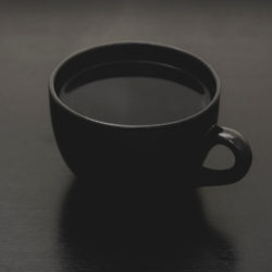 Schwarzer Kaffee in schwarzer Tasse auf dunkel grauem Tisch