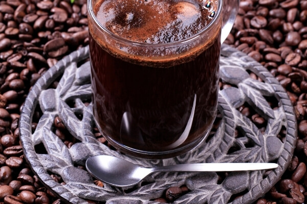 Schwarzerer Kaffee im Glas und Kaffeebohnen im Hintergrund