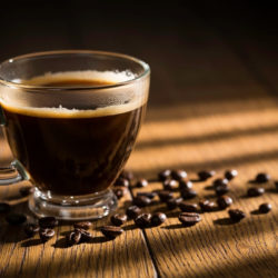 Schwarzer Kaffee mit Kaffeebohnen daneben im Licht und Schattenspiel auf einem Tisch