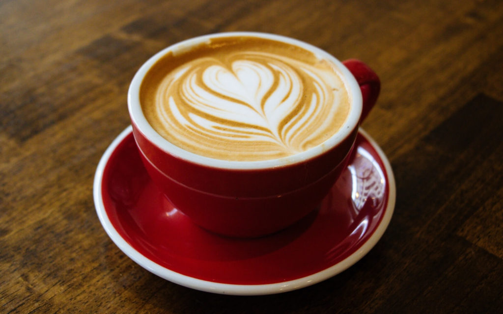 Cappuccino mit Latte Art in einer roten Tasse samt Untertasse
